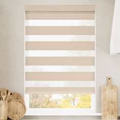 a kitchen window covered in beige and white striped roman blind blinds with wooden cutting boards next to it