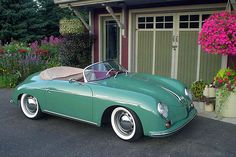 a green sports car parked in front of a house with pink flowers and potted plants