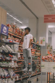 a man standing on top of a shopping cart talking on a cell phone in a grocery store