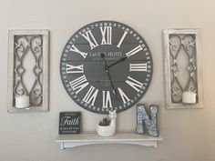 a large clock mounted to the side of a wall next to two small frames with candles