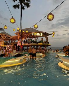 many people are in the water at an outdoor swimming pool with lights strung over it