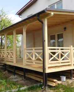 a wooden porch with railings on the front and side of a house in the background