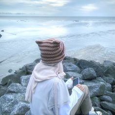 a person sitting on rocks looking out at the ocean with a book in their hand