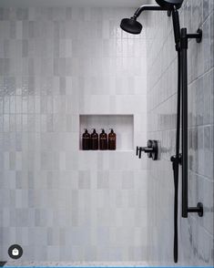 a white tiled shower with black fixtures and bottles on the shelf in the niche above it