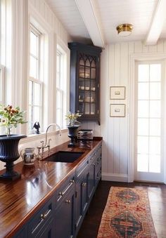 a kitchen with wooden counter tops next to two windows and a rug on the floor