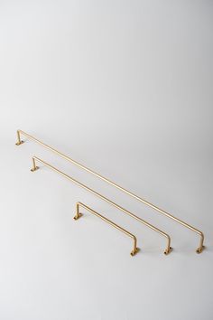 three brass - plated metal hooks hang on a white wall in the shape of two long bars