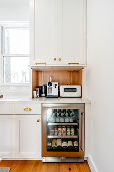 a kitchen with white cabinets and wood flooring has a wine cooler in the corner