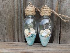 two glass bottles with shells in them sitting on a wooden table