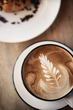 a cappuccino with a leaf drawn on it and a cookie in the background