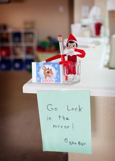 an elf is sitting on top of a desk with a note and pen in his hand