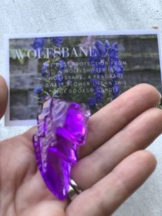 a person holding a purple crystal in their left hand and business card with the words wolfsbane on it