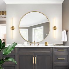 a bathroom with a large round mirror above the sink and two gold faucets