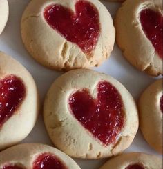 some heart shaped cookies are on a white plate with red jam in the middle and one has a bite taken out of it