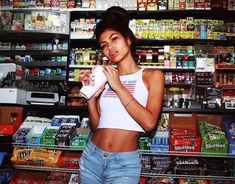 a woman standing in front of a grocery store holding a drink and chewing on a candy bar