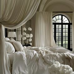 a bed with white sheets and pillows in front of a large window that has flowers on it