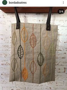 a bag hanging on a brick wall with leaves painted on it and leather handles in the front