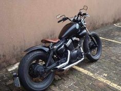 a black motorcycle parked on the side of a road next to a wall and sidewalk