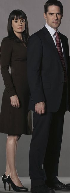 two people standing next to each other in front of a gray background with one person wearing a suit and tie