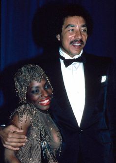 a man in a tuxedo standing next to a woman wearing a beaded dress