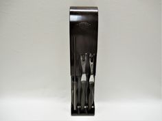 there are three forks and two knives in this black holder on the wall, with one fork sticking out of it's side