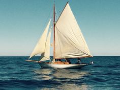 a sailboat with white sails is in the open water on a sunny day,