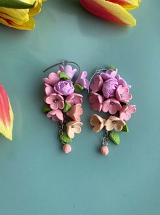 two pairs of earrings with flowers attached to them on a blue surface next to tulips