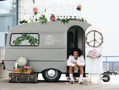 a man sitting in the doorway of a vintage camper trailer decorated with flowers and greenery