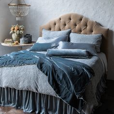 a bed with blue sheets and pillows next to a night stand on a wooden table