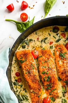 two salmon fillets in a skillet with tomatoes and spinach on the side