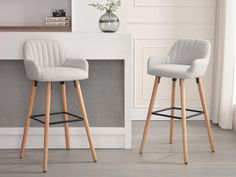 two white barstools with wooden legs in front of a fireplace and vase on the wall