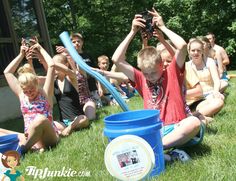 a group of people sitting on the grass holding up their hands to catch frisbees