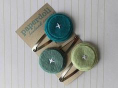 three small hair pins with green and blue felt on them, sitting on top of a piece of paper