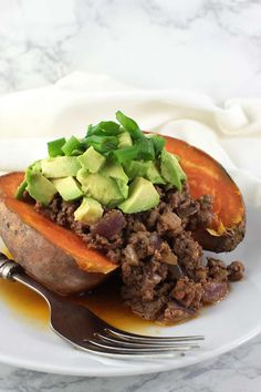 a white plate topped with a stuffed sweet potato covered in meat and avocado