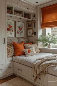 a white bed sitting under a window next to a wooden floor covered in lots of pillows