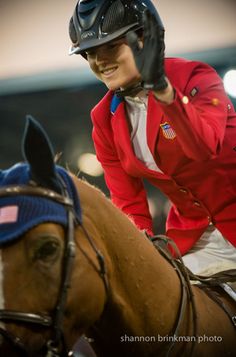 a woman in red jacket riding on the back of a brown and white horse at night