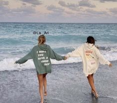 two girls walking on the beach holding hands and wearing sweatshirts that read, i hope you have a good day