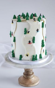 a white cake with trees and skiers on the top is sitting on a pedestal