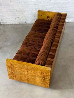 a couch that is sitting in the middle of some concrete flooring with a brick wall behind it