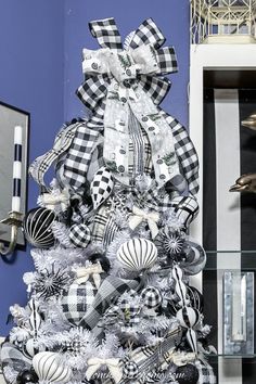 a white christmas tree with black and white ornaments on it in front of a blue wall