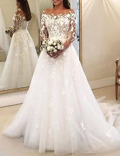 a woman standing in front of a mirror wearing a white wedding dress with long sleeves