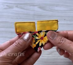 two hands are holding up a yellow and black flowered fabric piece that has been sewn onto