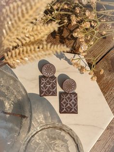 two wooden earrings sitting on top of a piece of paper next to a glass vase