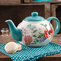 a teapot with flowers and polka dots sits on a napkin next to some cookies