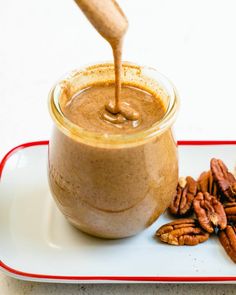 a glass jar filled with nut butter on top of a white plate next to pecans