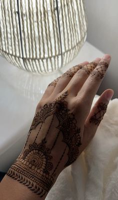 a woman's hand with henna tattoos on it and a lamp in the background