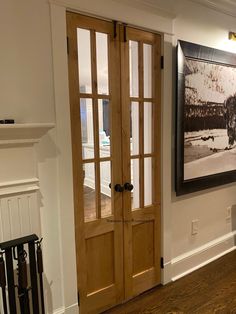 an empty living room with wood floors and white walls, two doors open to reveal a large painting on the wall