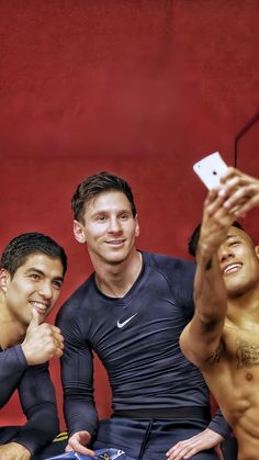 three men taking a selfie in front of a red wall with their cell phones