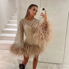 a woman taking a selfie wearing a dress with ostrich feathers on it