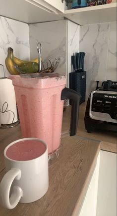 a pink smoothie in a white cup next to a blender on a counter