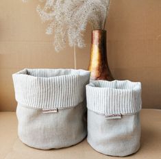 two white storage baskets sitting on top of a table next to a vase with dried flowers in it